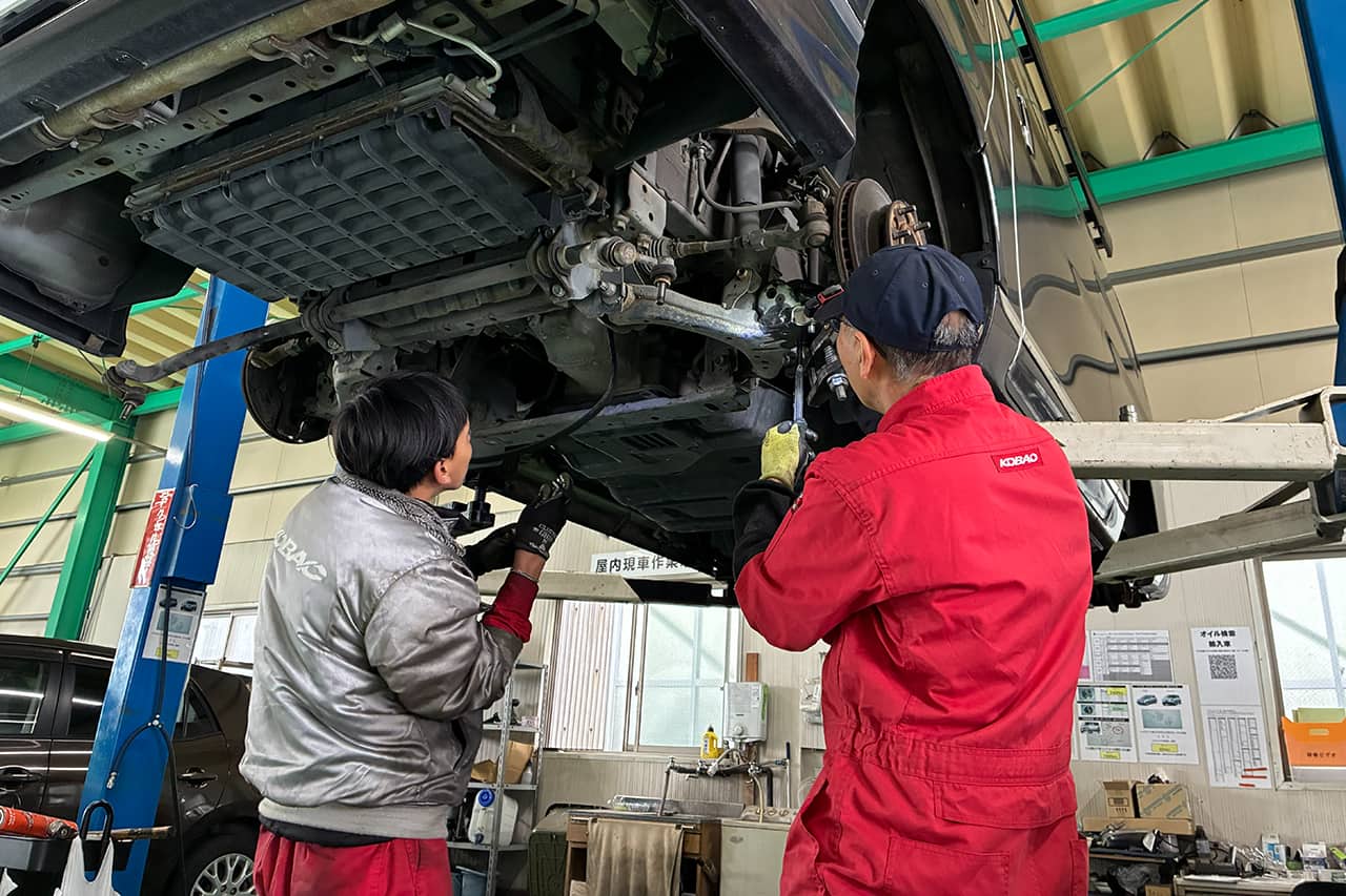 リフトアップされた車の下回りを点検する2人の整備士