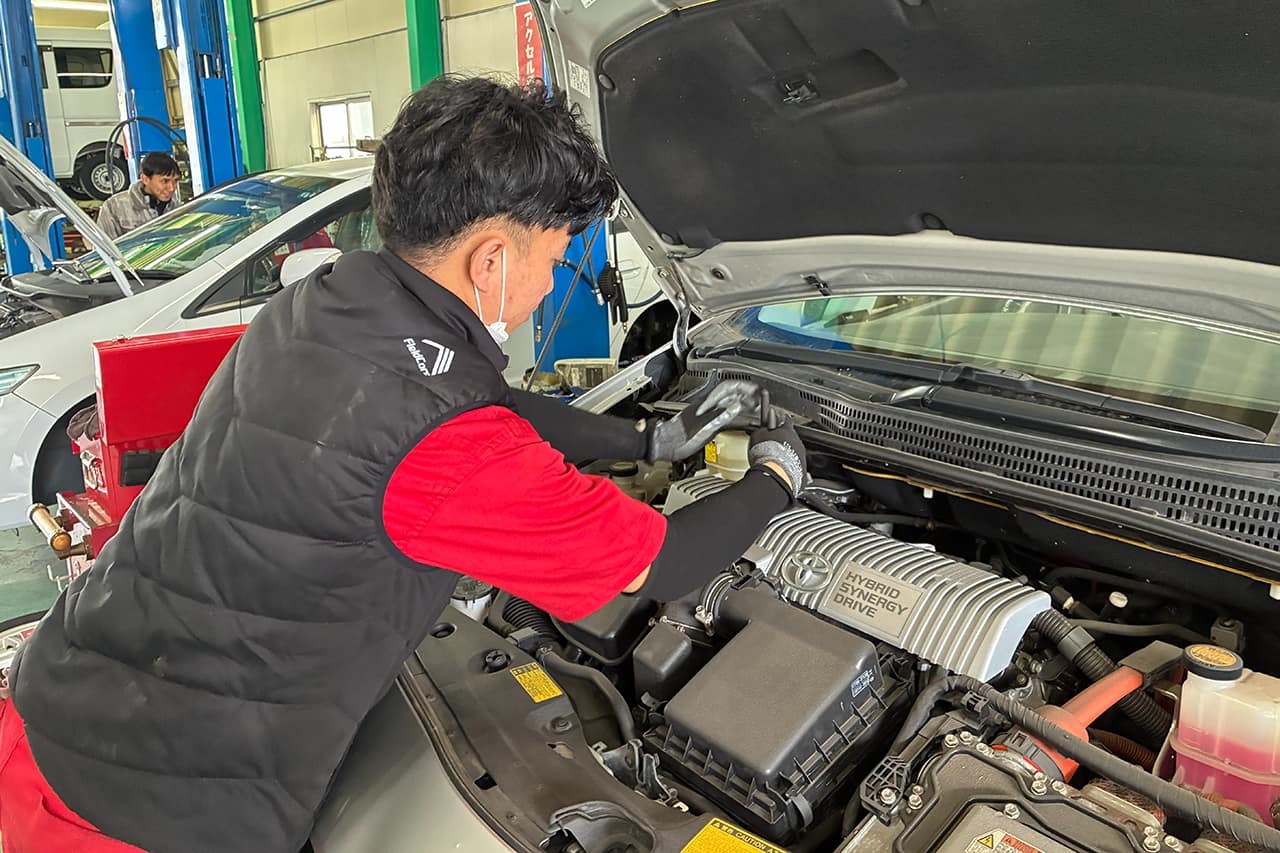 車のエンジンルームを点検する整備士